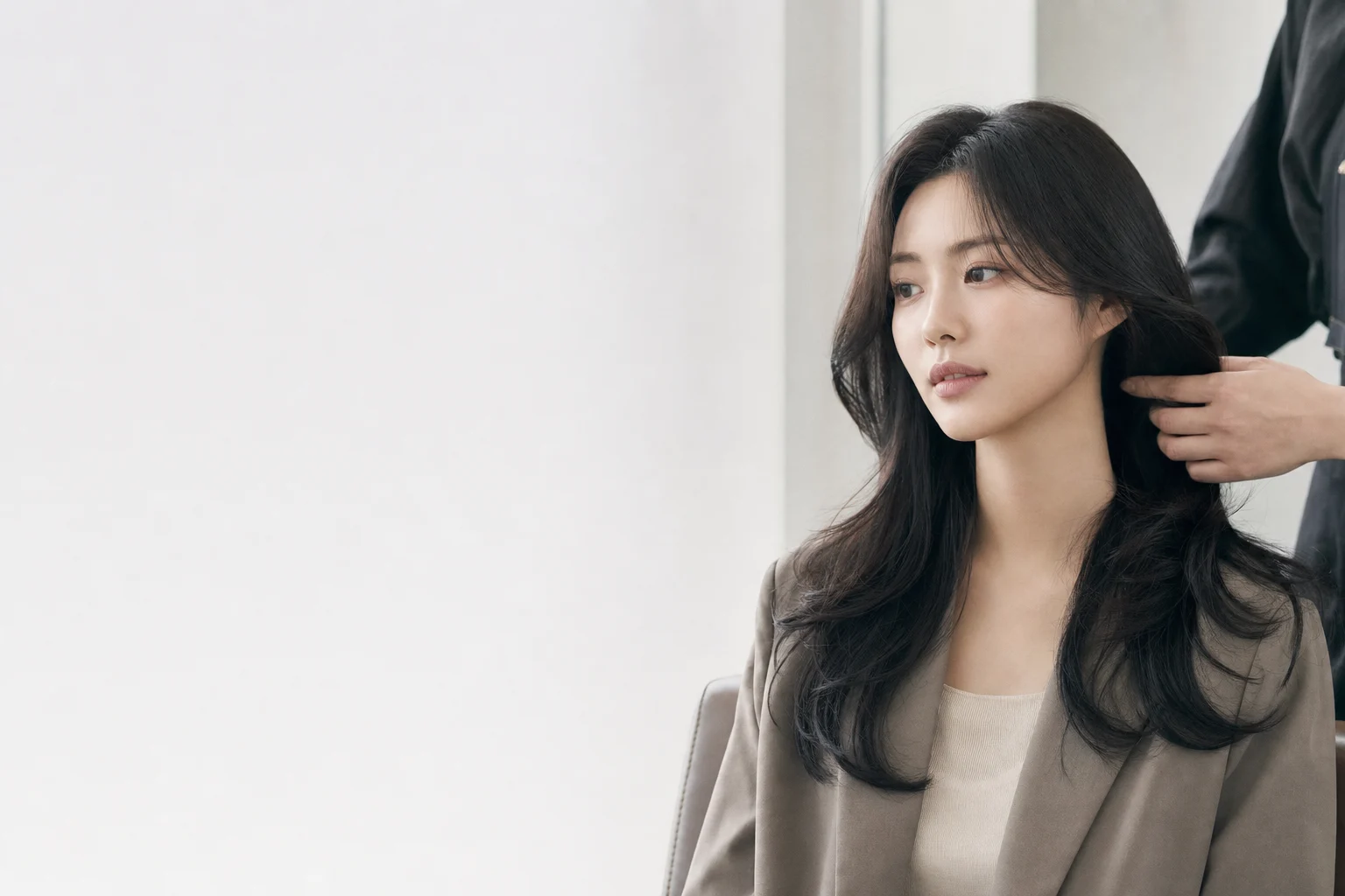 A young woman having her hair gently styled by a stylist in a serene, minimalist hair salon, softly lit.